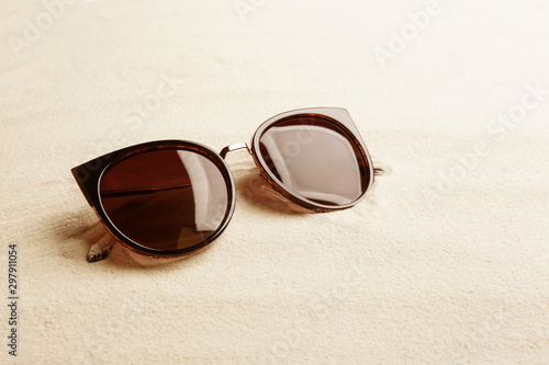 Stylish sunglasses on white sand, space for text. Summer time