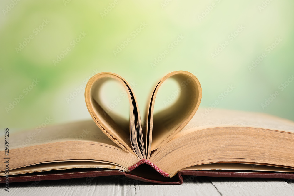 Open book on white wooden table against blurred green background, closeup Open book on white wooden table against blurred green background, closeup