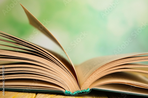 Open book on wooden table against blurred green background, closeup