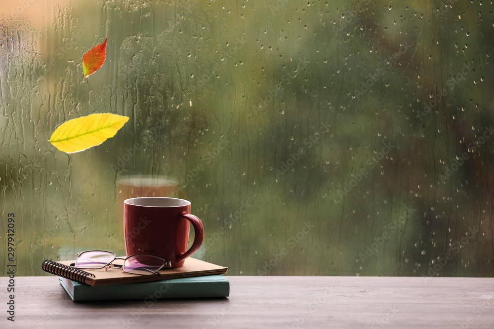 Composition with cup of drink and autumn leaf on windowsill, space for text. Rainy weather - obrazy, fototapety, plakaty 