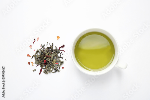 Green tea leaves and cup of hot beverage on white background, flat lay