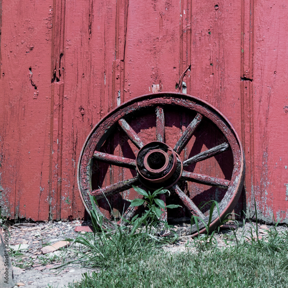An antique wagon wheel leaning against the wall of a red barn.  Vintage, rustic old wheel