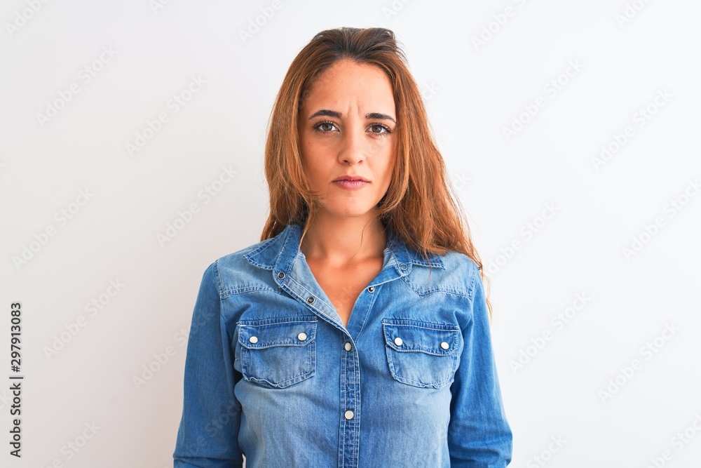 Young redhead woman wearing denim jacket standing over isolated background with serious expression on face. Simple and natural looking at the camera. Young redhead woman wearing denim jacket standing over isolated background with serious expression on face. Simple and natural looking at the camera.
