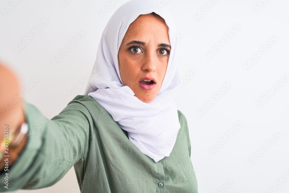 Young Arab woman wearing hijab taking selfie photo over isolated background scared in shock with a surprise face, afraid and excited with fear expression Young Arab woman wearing hijab taking selfie photo over isolated background scared in shock with a surprise face, afraid and excited with fear expression