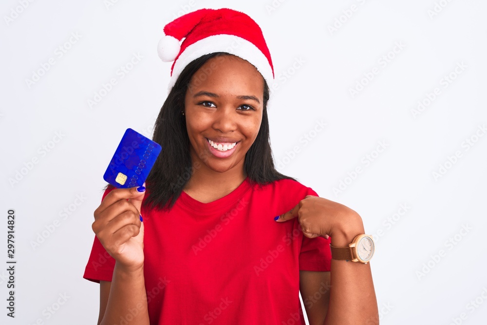 Young african american woman wearing christmas hat and holding credit card with surprise face pointing finger to himself Young african american woman wearing christmas hat and holding credit card with surprise face pointing finger to himself