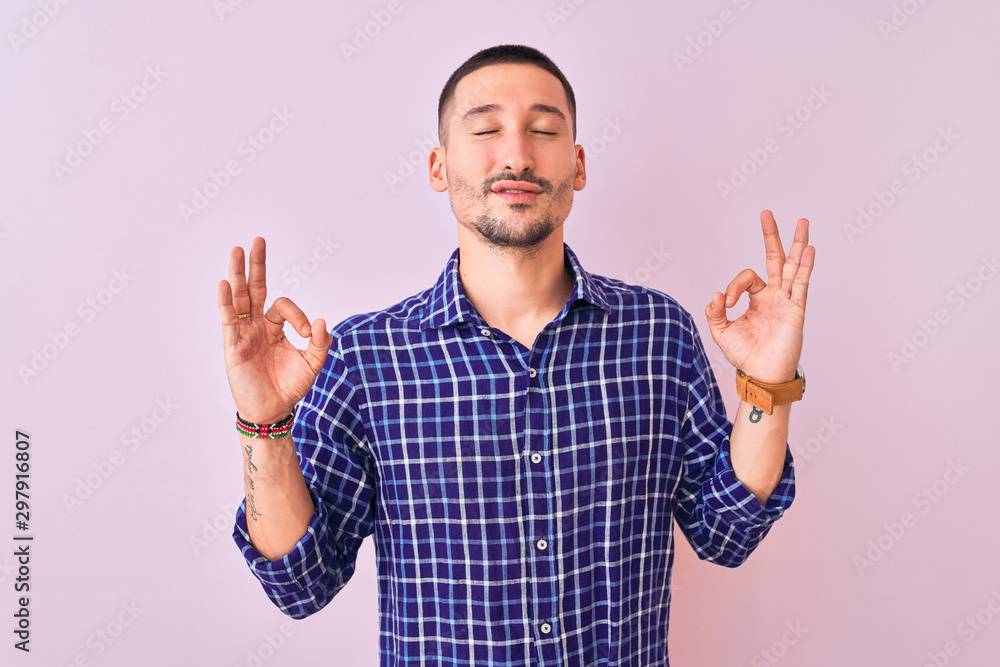 Fototapeta premium Young handsome man standing over isolated background relax and smiling with eyes closed doing meditation gesture with fingers. Yoga concept.