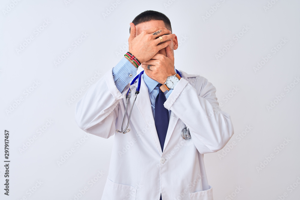 Young doctor man wearing stethoscope over isolated background Covering eyes and mouth with hands, surprised and shocked. Hiding emotion Young doctor man wearing stethoscope over isolated background Covering eyes and mouth with hands, surprised and shocked. Hiding emotion