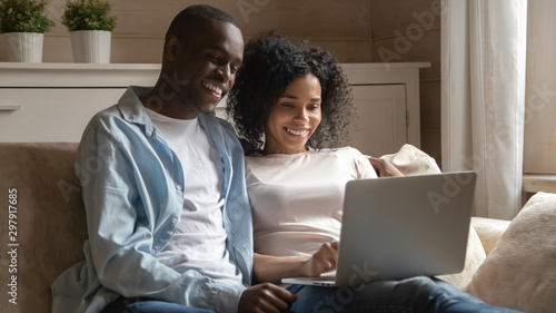 Happy mixed race family couple relaxing, watching movie on laptop.