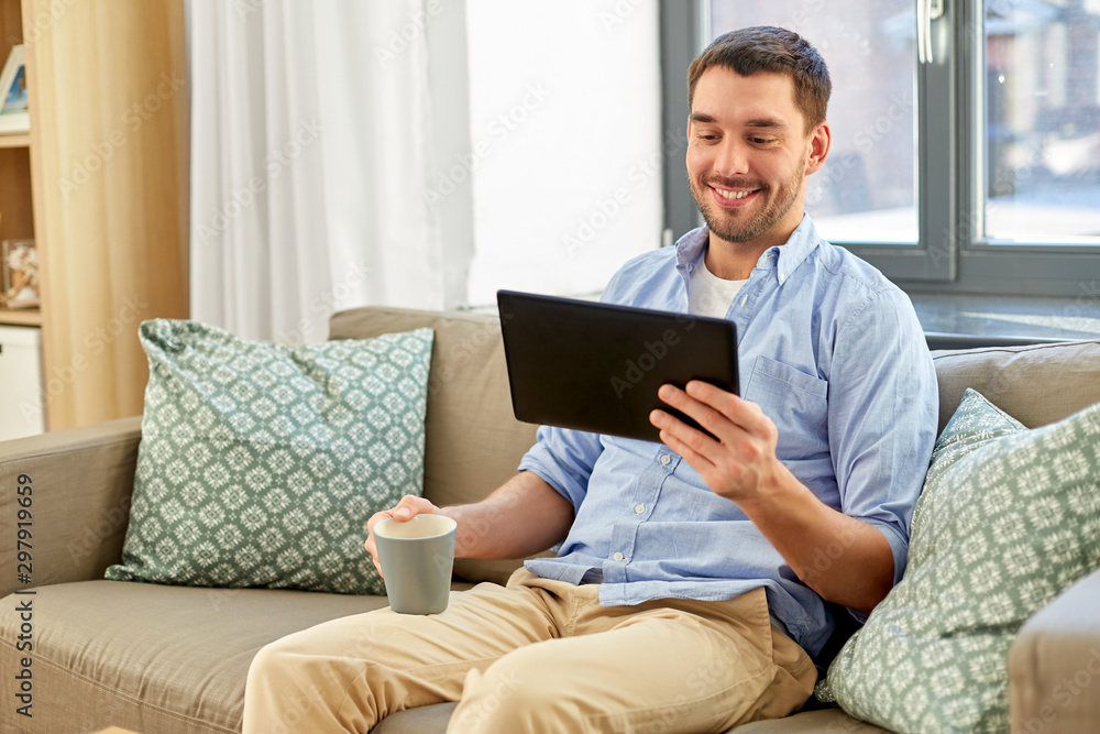 technology, people and lifestyle concept - happy man with tablet pc computer drinking coffee or tea at home