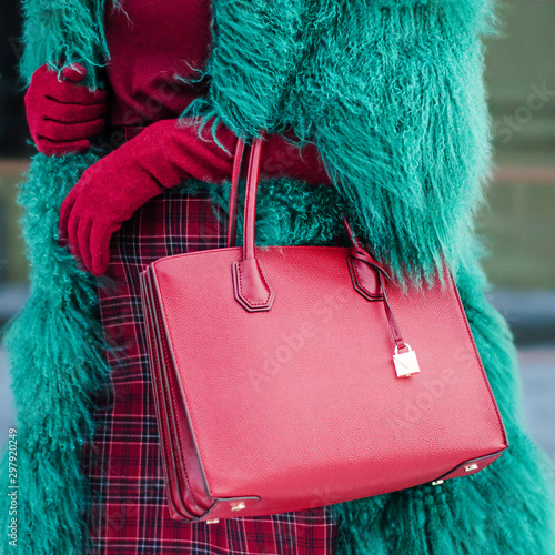 A woman in a green furry and warm fur coat in autumn or winter. Red burgundy bag. Fashionable bag close-up in female hands.Girl walks in the city outdoors. Stylish modern and feminine image, style.