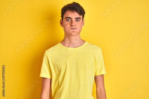 Teenager boy wearing yellow t-shirt over isolated background puffing cheeks with funny face. Mouth inflated with air, crazy expression.