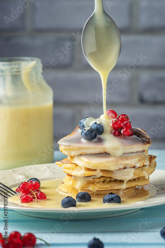 A stack of freshly prepared pancakes is poured with condensed milk. Tasty breakfast with fresh berries.