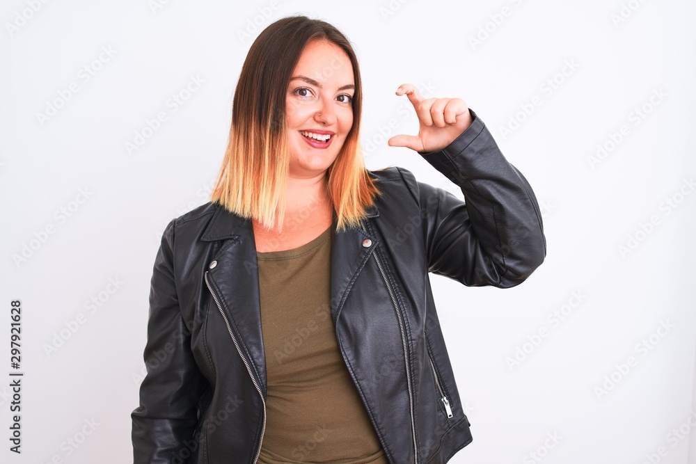 Young beautiful woman wearing t-shirt and jacket standing over isolated white background smiling and confident gesturing with hand doing small size sign with fingers looking and the camera. Young beautiful woman wearing t-shirt and jacket standing over isolated white background smiling and confident gesturing with hand doing small size sign with fingers looking and the camera.