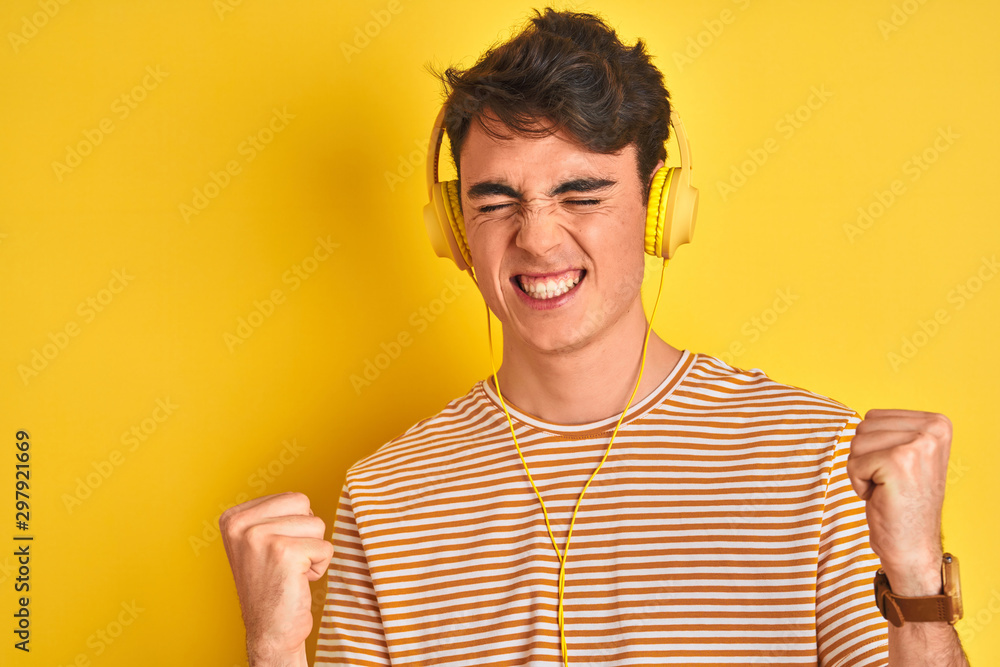 Teenager boy wearing headphones over isolated yellow background very happy and excited doing winner gesture with arms raised, smiling and screaming for success. Celebration concept. Teenager boy wearing headphones over isolated yellow background very happy and excited doing winner gesture with arms raised, smiling and screaming for success. Celebration concept.
