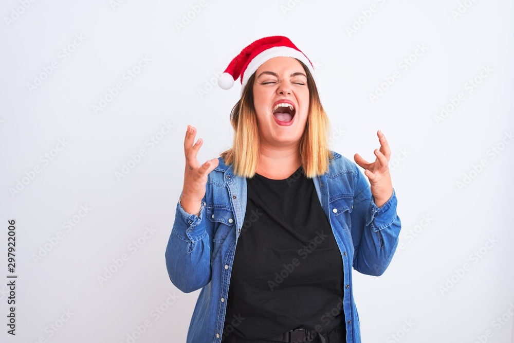 Young beautiful woman wearing Christmas Santa hat standing over isolated white background celebrating mad and crazy for success with arms raised and closed eyes screaming excited. Winner concept Young beautiful woman wearing Christmas Santa hat standing over isolated white background celebrating mad and crazy for success with arms raised and closed eyes screaming excited. Winner concept