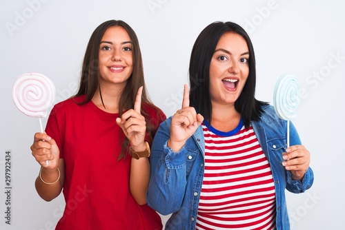 Young beautiful women holding sweet lollipop standing over isolated white background surprised with an idea or question pointing finger with happy face, number one