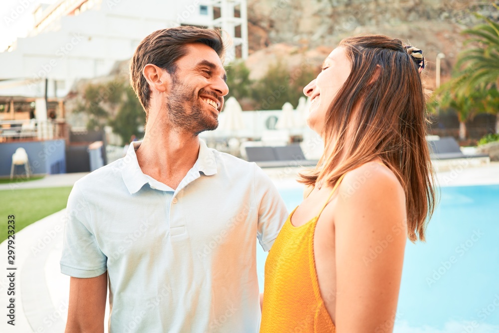 Young beautiful couple on vacation smiling happy and confident. Standing with smile on face hugging at the beach club Young beautiful couple on vacation smiling happy and confident. Standing with smile on face hugging at the beach club