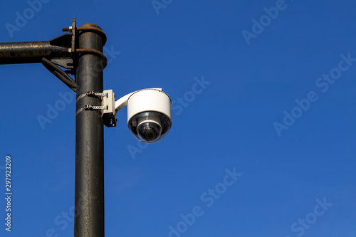 White street camera of external supervision installed on an outdoors pole against a blue sky. Modern CCTV camera, surveillance and monitoring.