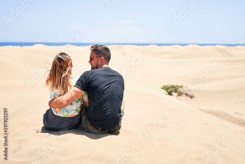 Young beautiful couple at sitting backwards and hugging at the beach