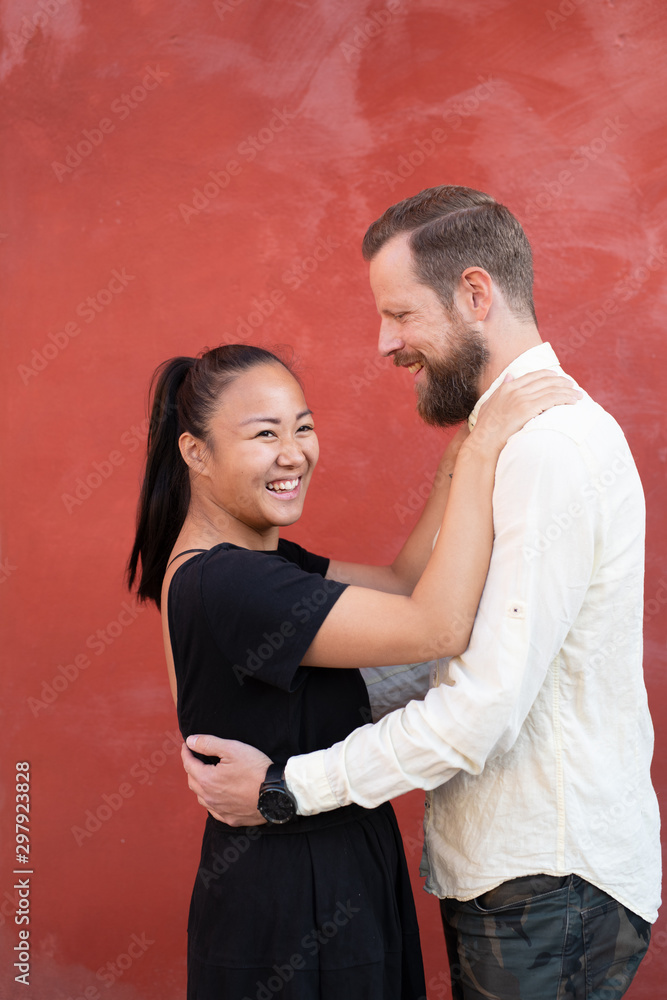 Interracial couple embraced by red wall