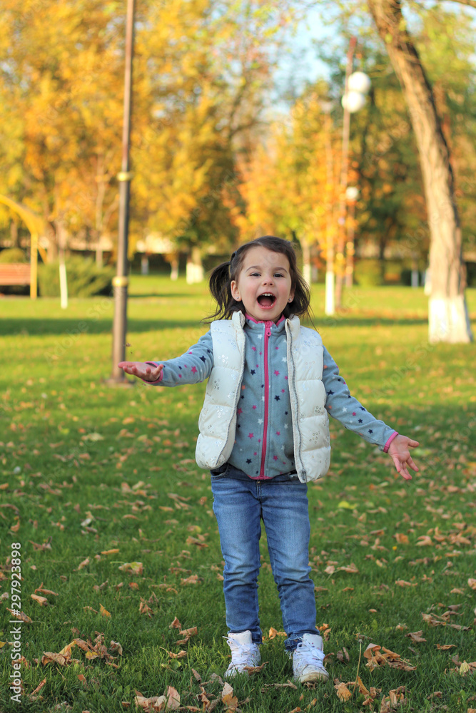 A merry child scatters an armful of yellow fallen leaves. Sunny sunset in autumn park outdoors A merry child scatters an armful of yellow fallen leaves. Sunny sunset in autumn park outdoors