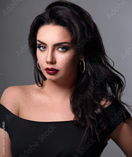 Beautiful bright makeup woman with long black curly volume black hair style, burgundy lipstick with vamp looking up on grey background.