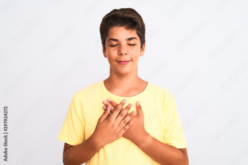 Handsome teenager boy standing over white isolated background smiling with hands on chest with closed eyes and grateful gesture on face. Health concept. Handsome teenager boy standing over white isolated background smiling with hands on chest with closed eyes and grateful gesture on face. Health concept.