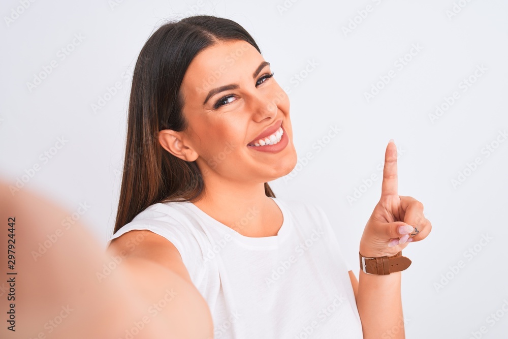 Beautiful young woman taking a selfie photo using smartphone over white background surprised with an idea or question pointing finger with happy face, number one Beautiful young woman taking a selfie photo using smartphone over white background surprised with an idea or question pointing finger with happy face, number one