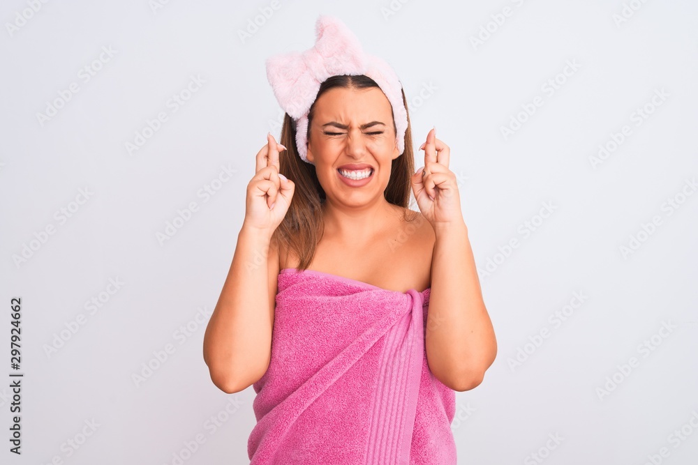 Beautiful young woman wearing pink shower towel and beauty headband over white background gesturing finger crossed smiling with hope and eyes closed. Luck and superstitious concept. Beautiful young woman wearing pink shower towel and beauty headband over white background gesturing finger crossed smiling with hope and eyes closed. Luck and superstitious concept.