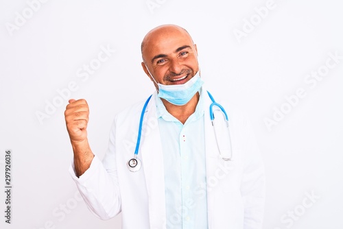 Middle age doctor man wearing stethoscope and mask over isolated white background smiling with happy face looking and pointing to the side with thumb up.