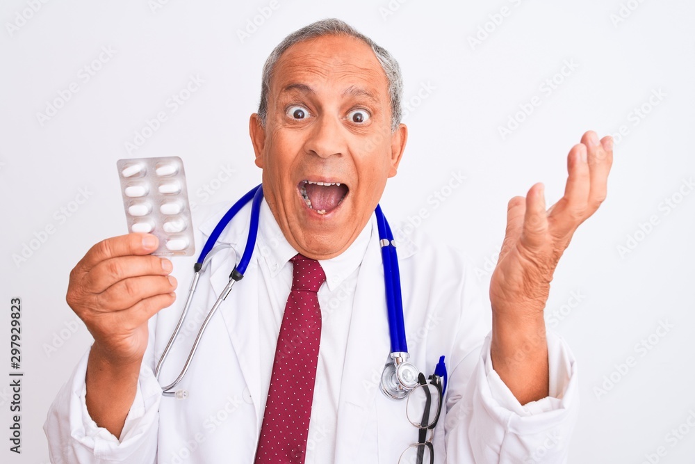 Senior doctor man wearing stethoscope holding pills over isolated white background very happy and excited, winner expression celebrating victory screaming with big smile and raised hands Senior doctor man wearing stethoscope holding pills over isolated white background very happy and excited, winner expression celebrating victory screaming with big smile and raised hands