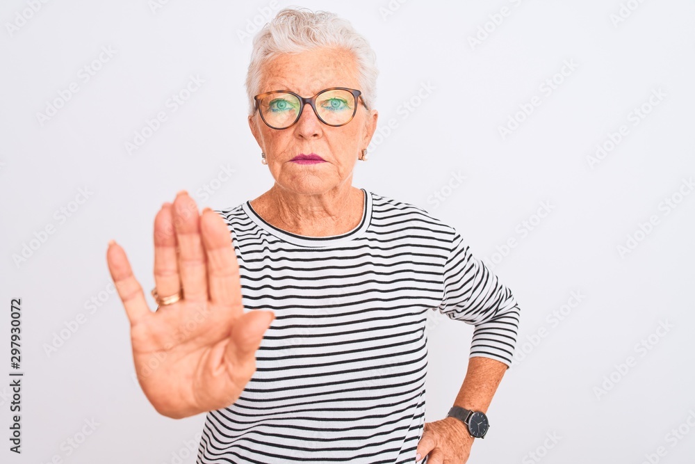 Senior grey-haired woman wearing striped navy t-shirt glasses over isolated white background doing stop sing with palm of the hand. Warning expression with negative and serious gesture on the face. Senior grey-haired woman wearing striped navy t-shirt glasses over isolated white background doing stop sing with palm of the hand. Warning expression with negative and serious gesture on the face.