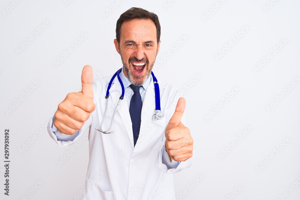 Middle age doctor man wearing coat and stethoscope standing over isolated white background approving doing positive gesture with hand, thumbs up smiling and happy for success. Winner gesture. Middle age doctor man wearing coat and stethoscope standing over isolated white background approving doing positive gesture with hand, thumbs up smiling and happy for success. Winner gesture.