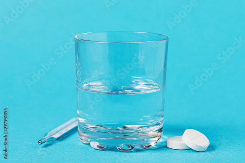 Thermometer, glass of water and pills on a blue background. Concept on the topic of medication