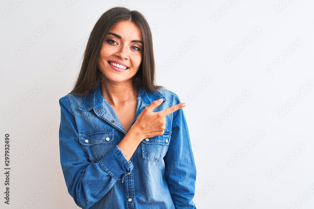 Young beautiful woman wearing casual denim shirt standing over isolated white background cheerful with a smile of face pointing with hand and finger up to the side with happy and natural expression Young beautiful woman wearing casual denim shirt standing over isolated white background cheerful with a smile of face pointing with hand and finger up to the side with happy and natural expression