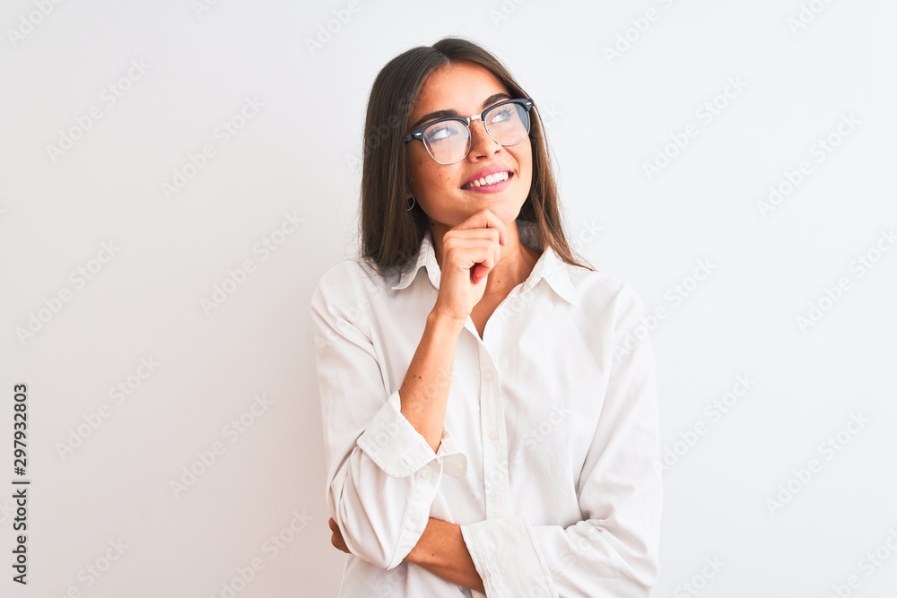 Young beautiful businesswoman wearing glasses standing over isolated white background with hand on chin thinking about question, pensive expression. Smiling and thoughtful face. Doubt concept. Young beautiful businesswoman wearing glasses standing over isolated white background with hand on chin thinking about question, pensive expression. Smiling and thoughtful face. Doubt concept.