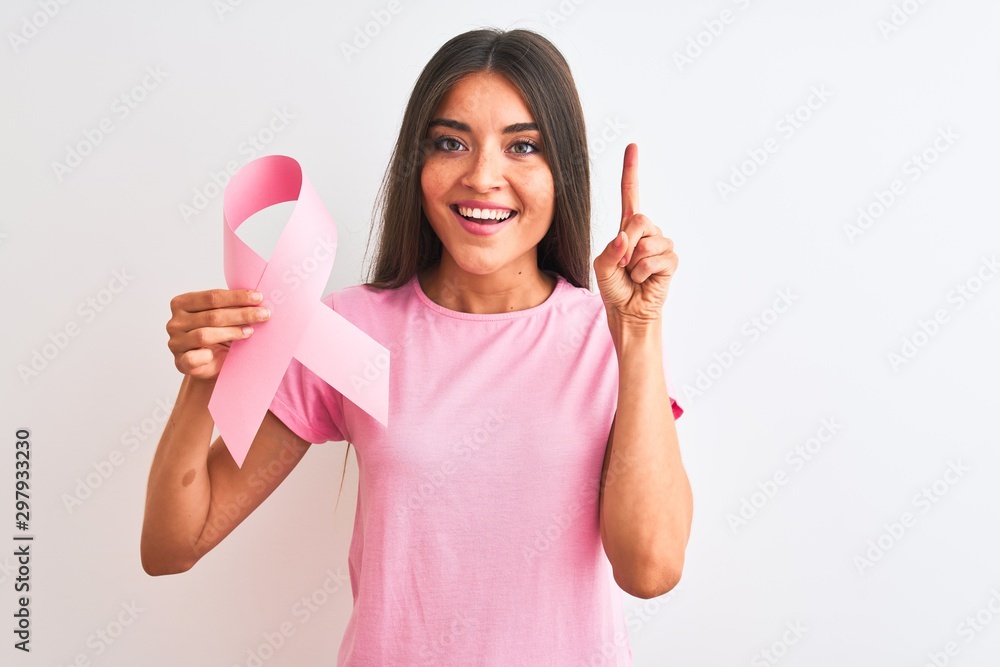 Young beautiful woman holding cancer ribbon standing over isolated white background surprised with an idea or question pointing finger with happy face, number one Young beautiful woman holding cancer ribbon standing over isolated white background surprised with an idea or question pointing finger with happy face, number one
