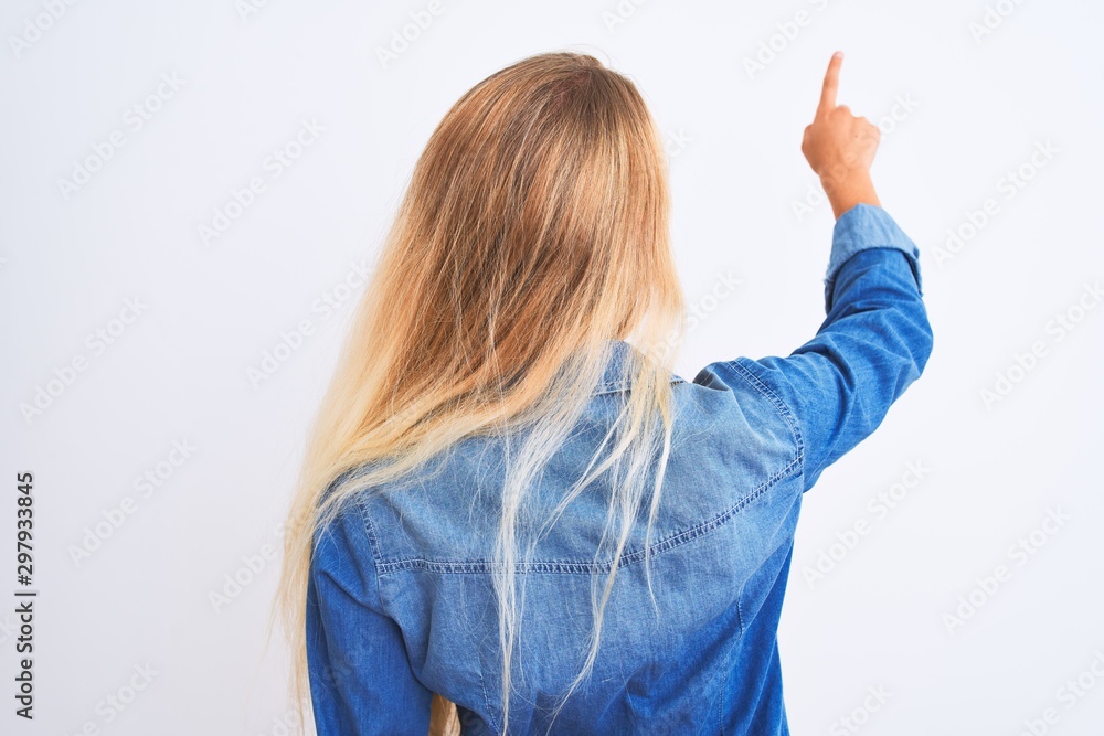 Young beautiful woman wearing casual denim shirt standing over isolated white background Posing backwards pointing ahead with finger hand Young beautiful woman wearing casual denim shirt standing over isolated white background Posing backwards pointing ahead with finger hand