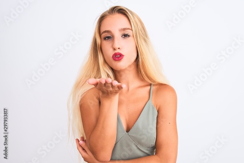 Young beautiful woman wearing casual green t-shirt standing over isolated white background looking at the camera blowing a kiss with hand on air being lovely and sexy. Love expression.