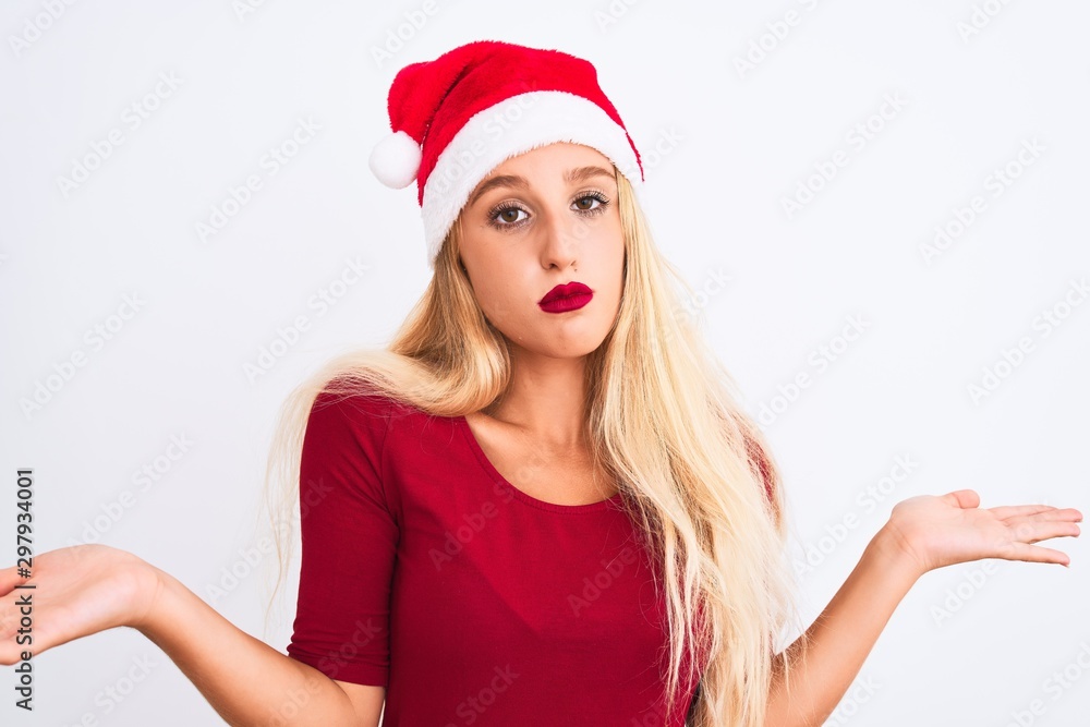 Young beautiful woman wearing Christmas Santa hat over isolated white background clueless and confused expression with arms and hands raised. Doubt concept. Young beautiful woman wearing Christmas Santa hat over isolated white background clueless and confused expression with arms and hands raised. Doubt concept.