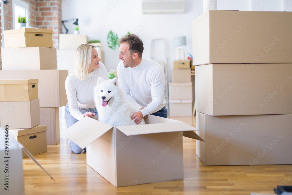 Fototapeta premium Young beautiful couple with dog sitting on the floor at new home around cardboard boxes