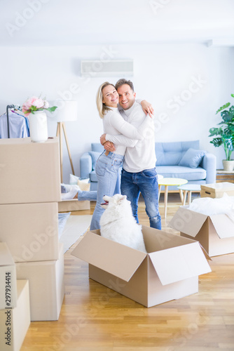 Young beautiful couple with dog hugging at new home around cardboard boxes © Krakenimages.com