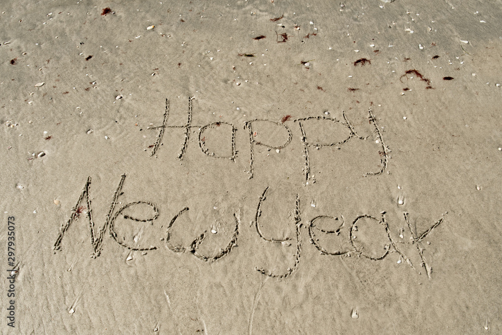 Fototapeta premium Happy New Year written in the sand at beach in Florida. New Year vacation in the sun concept. Seasons greetings. Sand with shells.