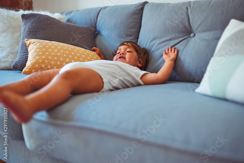 Beautiful toddler child girl wearing white bodysuit lying down on the sofa