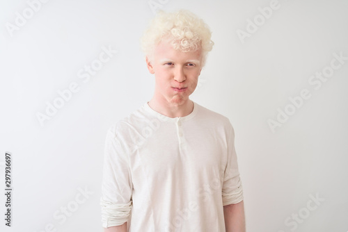 Young albino blond man wearing casual t-shirt standing over isolated white background puffing cheeks with funny face. Mouth inflated with air, crazy expression.