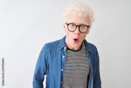 Young albino blond man wearing denim shirt and glasses over isolated white background afraid and shocked with surprise and amazed expression, fear and excited face.
