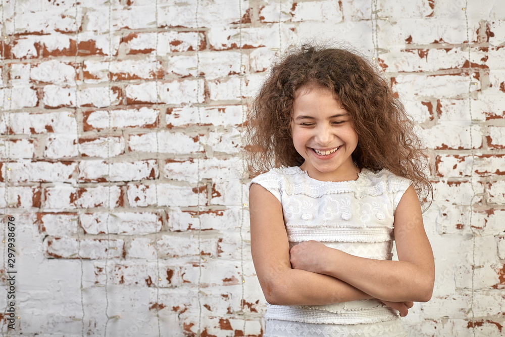 Young joyful girl smiling shyly over a brick wall crossed her arms relaxed