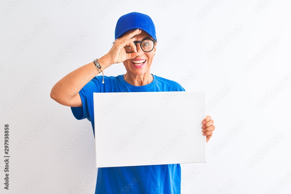 Senior deliverywoman wearing cap and glasses holding banner over isolated white background with happy face smiling doing ok sign with hand on eye looking through fingers Senior deliverywoman wearing cap and glasses holding banner over isolated white background with happy face smiling doing ok sign with hand on eye looking through fingers