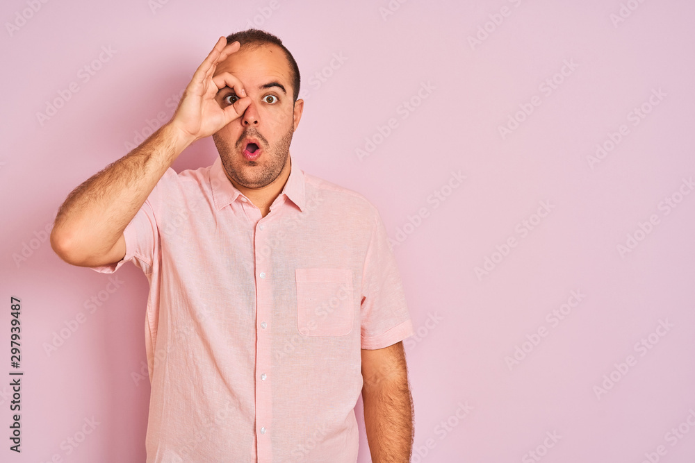 Young man wearing elegant shirt standing over isolated pink background doing ok gesture shocked with surprised face, eye looking through fingers. Unbelieving expression. Young man wearing elegant shirt standing over isolated pink background doing ok gesture shocked with surprised face, eye looking through fingers. Unbelieving expression.