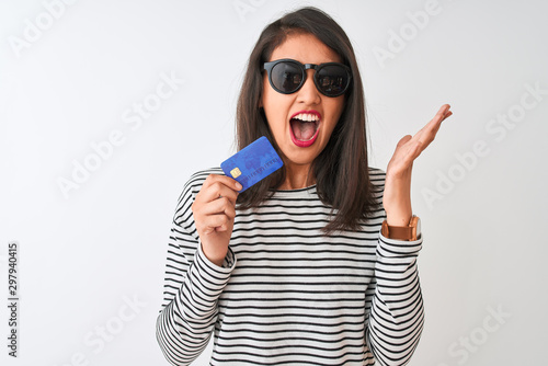 Young chinese woman wearing sunglasses holding credit card over isolated white background very happy and excited, winner expression celebrating victory screaming with big smile and raised hands